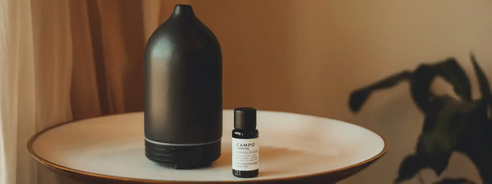 Black ceramic essential oil diffuser with a bottle of essential oil beside it.