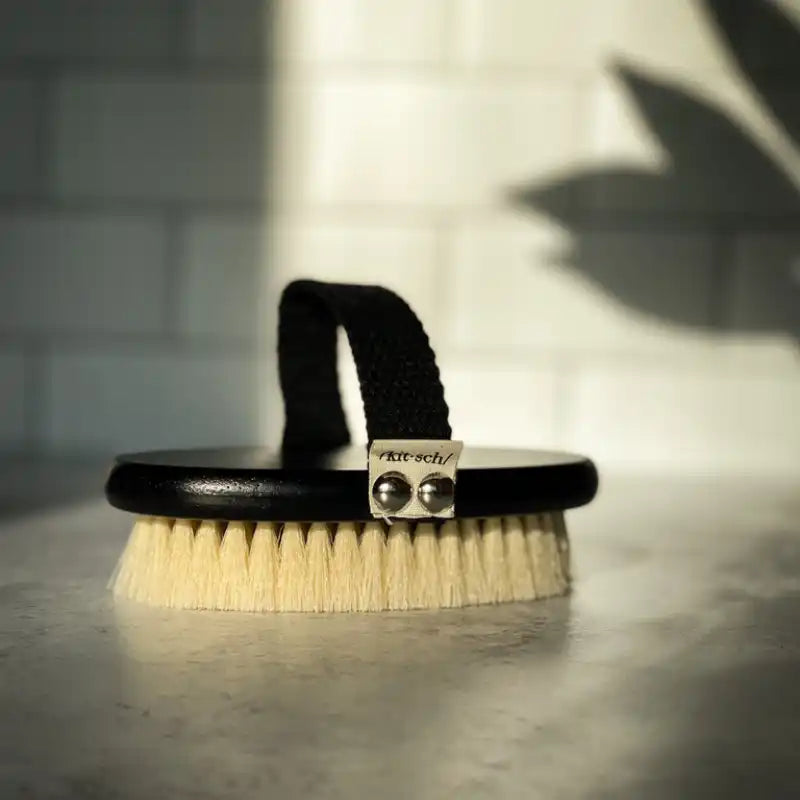 Oval-shaped brush with natural bristles and a black leather strap handle.