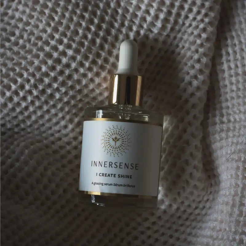 White glass bottle with gold accents labeled ’Innersense I Create Shine’ and a dropper top.